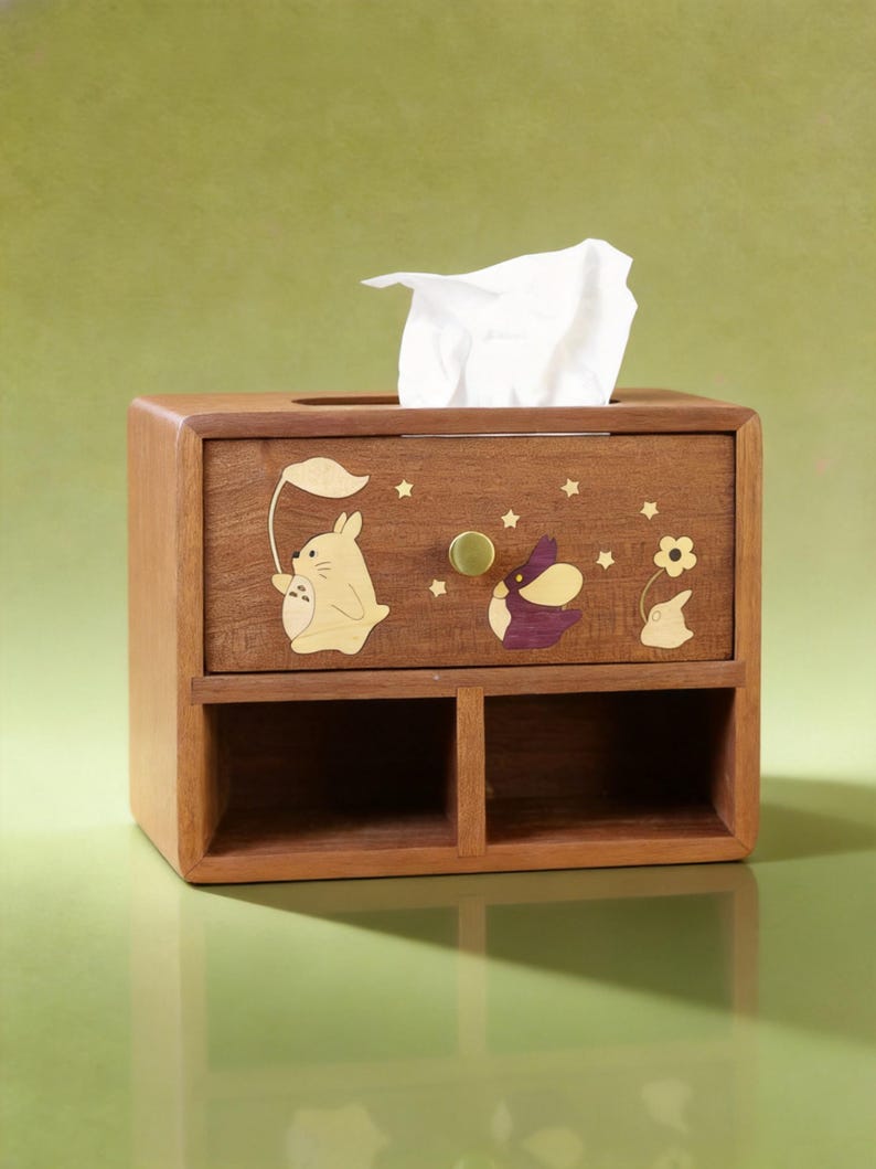 K&ouml;nnte beinhalten: Braune Holz-Taschentuchbox mit Schublade und zwei F&auml;chern. Die Box ist mit Ausschnitten von Zeichentrickfiguren und Sternen verziert. Ein wei&szlig;es Taschentuch ragt aus der oberen &Ouml;ffnung heraus. Die Schublade hat einen goldfarbenen Knopf.