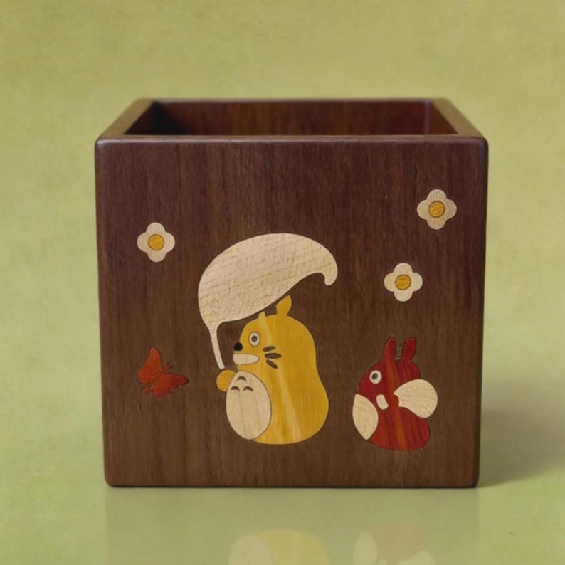 May include: A wooden square box with a dark brown finish. The box is decorated with inlaid wood designs of a yellow character with a white umbrella, a red character, a red butterfly, and white flowers.