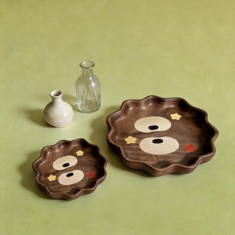 May include: Two wooden decorative trays with a wavy edge and a bear face design. The bear face is made of light wood and black ovals for eyes. The trays have yellow star and red heart accents.