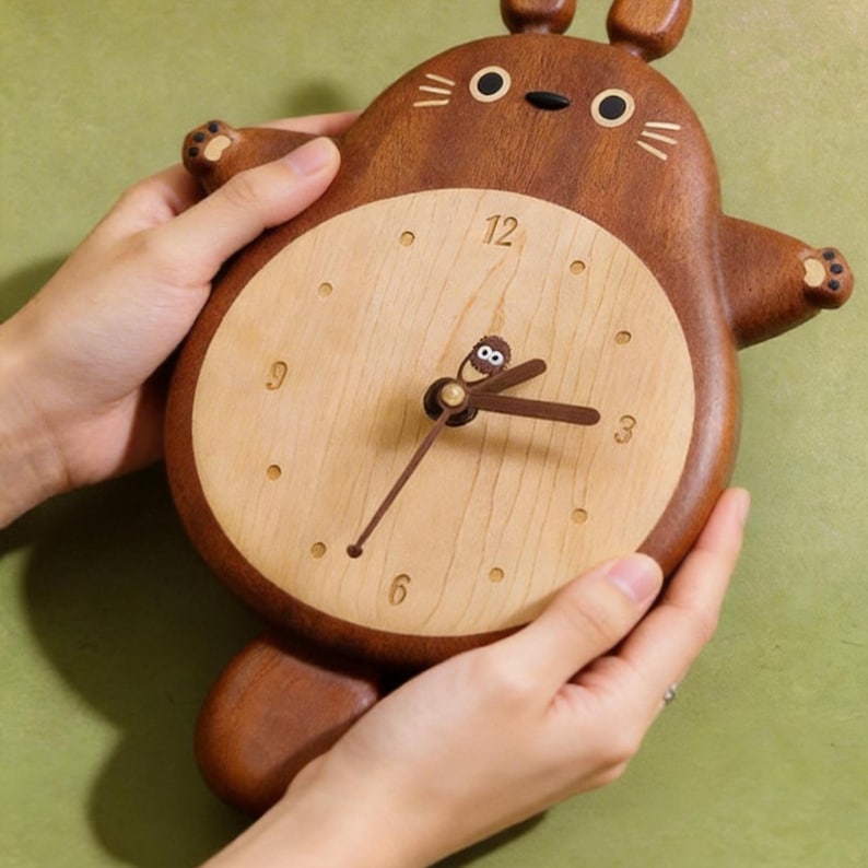May include: A wooden wall clock in the shape of a cartoon character. The clock has a light wood face with dark brown hands and hour markers. The outer frame is a darker brown, with the character's features carved into the wood.