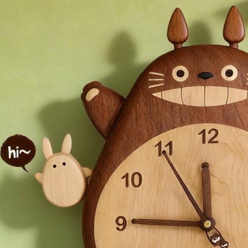 May include: A wooden wall clock shaped like a large brown creature with pointed ears, a wide smiling mouth, and a light-coloured belly featuring black numbers. A small light-coloured figure stands to the left with a speech bubble containing the text hi~.