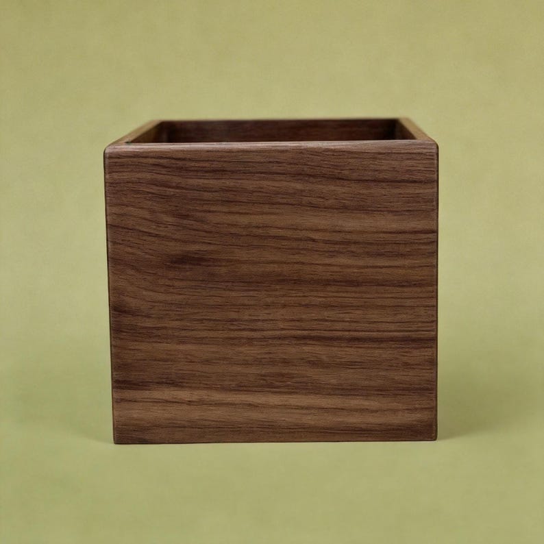 May include: A square wooden box with a rich brown finish. The box has a smooth, polished surface and a simple, minimalist design. The open top reveals the hollow interior, perfect for storage or display.