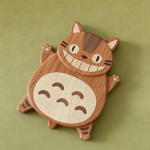 May include: Wooden cat-shaped coaster with a smiling face and a light-colored belly. The coaster is made of light and dark brown wood, with details like paws and stripes. The design is a cartoon cat.
