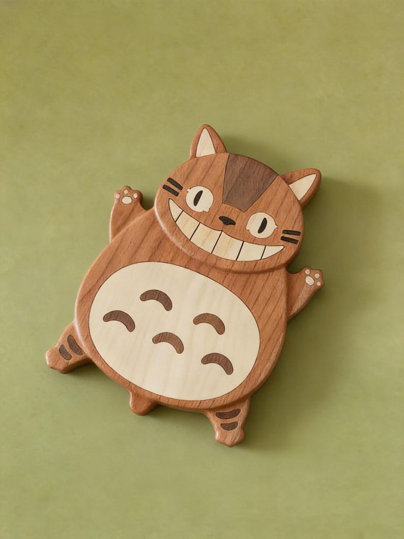 May include: Wooden cat-shaped coaster with a smiling face and a light-colored belly. The coaster is made of light and dark brown wood, with details like paws and stripes. The design is a cartoon cat.
