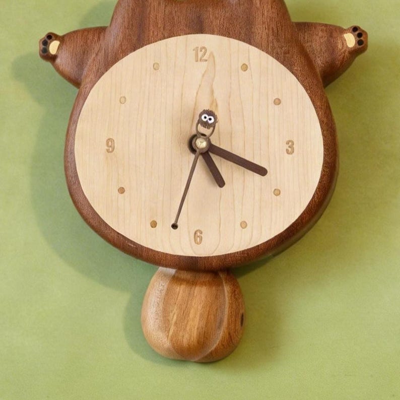 May include: A wooden bear-shaped wall clock with a light-colored face and dark brown hands. The clock has a pendulum and is made of natural wood tones. The clock face features the numbers 12, 3, 6, and 9.