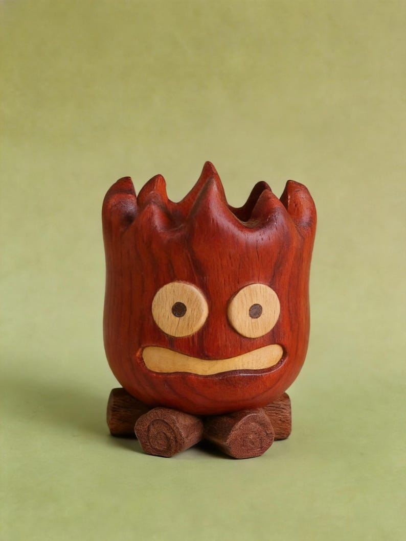 May include: A handcrafted wooden planter shaped like a cartoon character with a fiery appearance. The planter is primarily reddish-brown with lighter wood accents for the eyes and mouth. It sits on a base made of small wooden logs.
