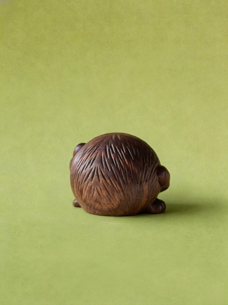 Puede incluir: Peque&ntilde;a escultura redonda de madera de un animal, posiblemente un erizo o criatura similar, con detalles tallados. La escultura es marr&oacute;n y se asienta sobre un fondo verde. El tallado muestra la textura del pelaje del animal.