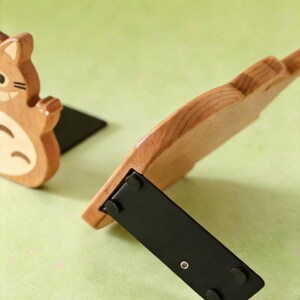 May include: Wooden bookends featuring a cartoon squirrel design. The bookends are made of light brown wood with black bases. One bookend is upright, while the other is tilted, showcasing the design and construction. The background is a light green color.