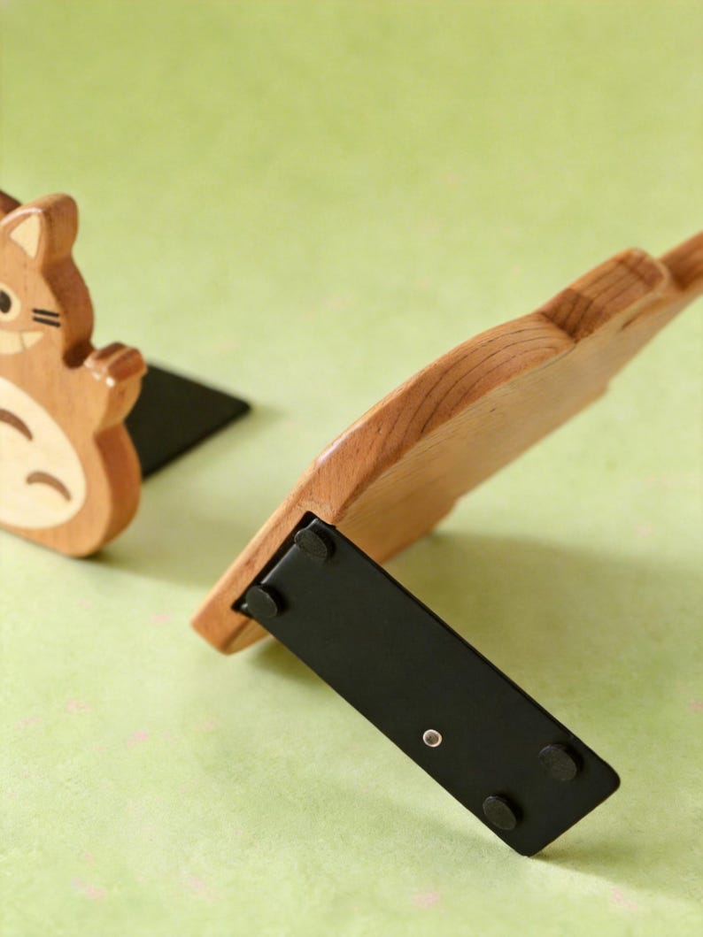 May include: Wooden bookends featuring a cartoon squirrel design. The bookends are made of light brown wood with black bases. One bookend is upright, while the other is tilted, showcasing the design and construction. The background is a light green color.