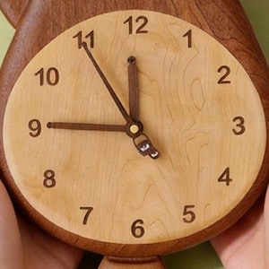 May include: A round wall clock featuring a light-coloured wooden face with dark brown numerals from one to twelve. The clock has dark brown hour, minute, and second hands. The outer frame of the clock is crafted from a darker, rich brown wood.