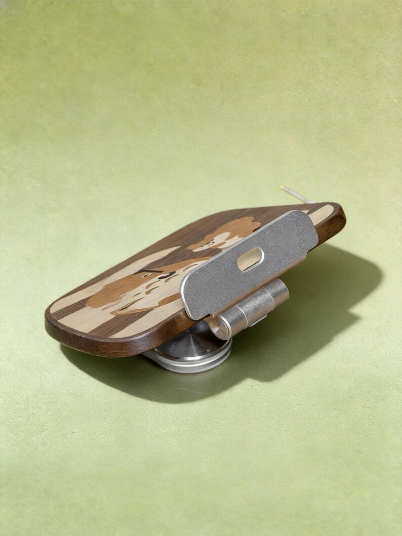 May include: A wooden phone stand featuring a dark and light wood inlay design of a dog's face. The stand includes a silver-colored metal adjustable hinge and a circular base, allowing for multiple viewing angles for a mobile device.