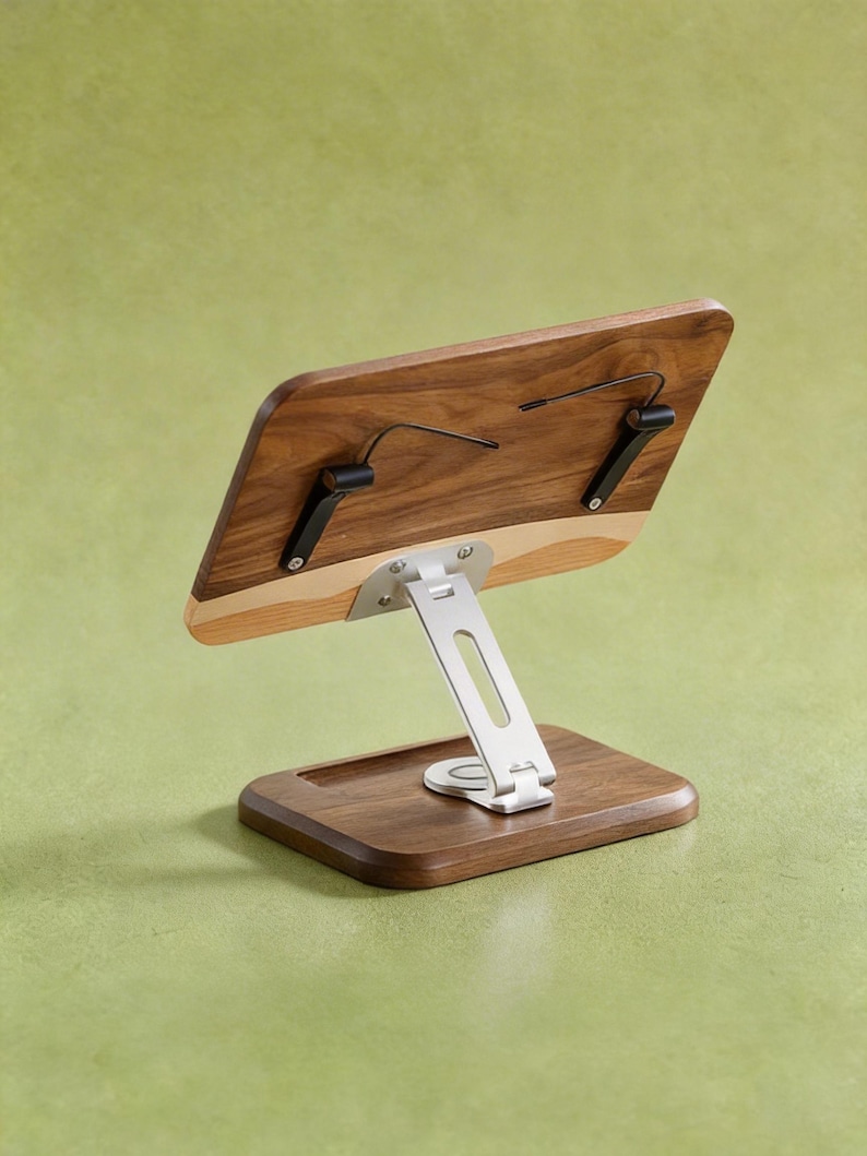 May include: A wooden tablet or book stand featuring a dark walnut wood rectangular base and a matching adjustable back panel. The stand includes a silver-colored metal support arm and two black metal clips attached to the back panel for holding items.