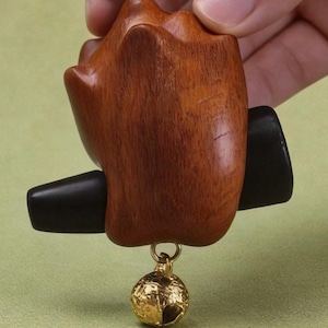 May include: A wooden bottle stopper with a dark brown finish and a black rubber insert. A small, gold-colored, textured ball hangs from the stopper. The stopper is designed to fit into a bottle.
