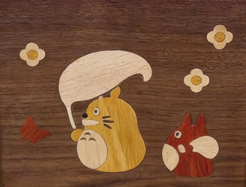 May include: Wooden inlay art featuring a cartoon character holding a leaf umbrella, with a smaller character to the right. The artwork includes flower and leaf accents, all set against a dark wood background. The characters are in shades of yellow and red.