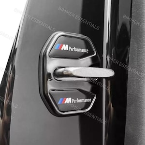 May include: Black car door latch cover with the text "M Performance" and the BMW logo in blue, red, and white. The cover is black with a silver latch.
