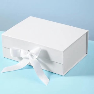 May include: A white gift box with a white satin ribbon tied in a bow. The box is closed and has a flap on the top.