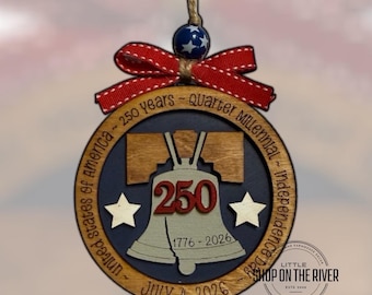 May include: Wooden ornament celebrating 250 years of American independence. The design features the Liberty Bell, the number 250, and the dates 1776-2026. It includes the text "July 4, 2026" and is adorned with a red ribbon.
