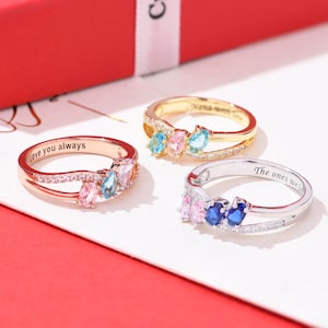 Peut inclure: Trois bagues personnalisées avec des pierres précieuses colorées. L'une est en or rose avec l'inscription "Love you always". Une autre est en or avec l'inscription "Nana with love". La troisième est en argent avec l'inscription "The ones we".