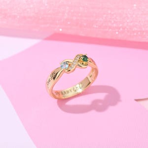 May include: Gold infinity ring with two gemstones, one green and one blue, and the inscription "Baby Boy" and "Baby Girl".