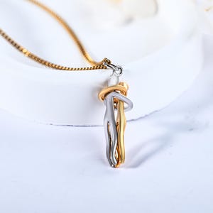 Op de afbeelding: Een gouden en zilveren ketting met een hanger van twee figuren die elkaar in een omhelzing vasthouden.
