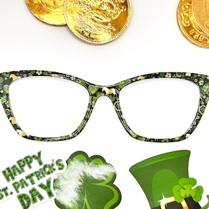May include: Green cat-eye glasses with a shamrock and horse print. The glasses are on a white background with gold coins and St. Patrick's Day decorations.