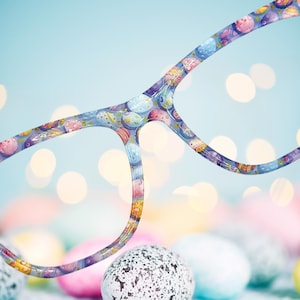 May include: A pair of blue glasses with a colorful pattern of planets and stars. The glasses are in focus, while the background is blurred and out of focus.
