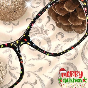 May include: Black eyeglasses with a colorful light pattern on the frame. The glasses are on a white background with a silver glitter pattern.