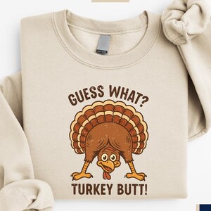 A beige sweatshirt with a graphic of a turkey and the text "Guess What? Turkey Butt!" printed on it.