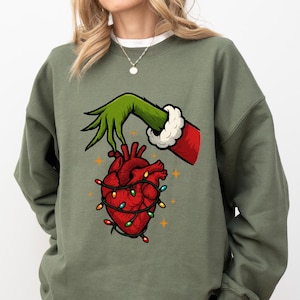 A person wearing a green sweatshirt with a graphic of a hand holding a heart with Christmas lights.