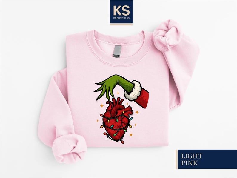 A pink sweatshirt with a graphic design depicting a hand holding a lit heart, surrounded by Christmas lights.