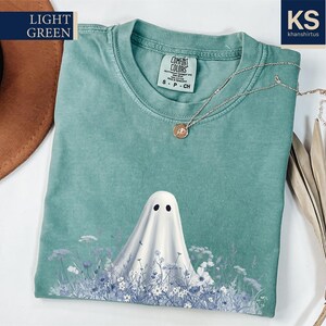 a light green t-shirt with a ghost design printed on it, along with a brown hat and some dried flowers.