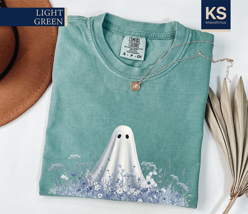 a light green t-shirt with a ghost design printed on it, along with a brown hat and some dried flowers.