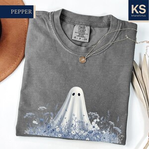 a gray t-shirt with a ghost design printed on it, along with a hat and some dried flowers.