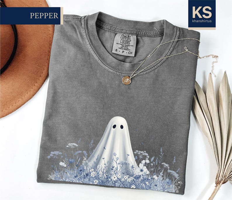 a gray t-shirt with a ghost design printed on it, along with a hat and some dried flowers.