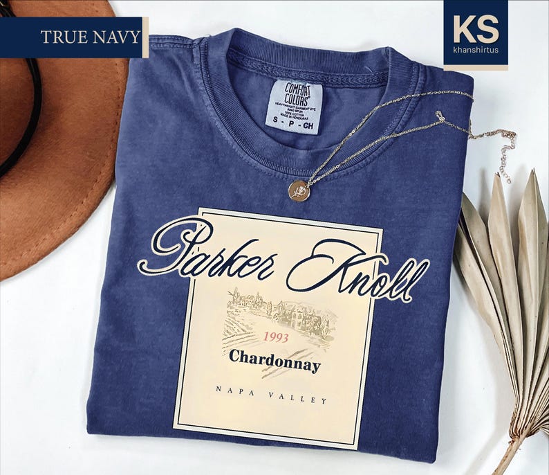 a navy blue t-shirt with a wine label design, a brown hat, and some dried leaves, all placed on a white background.