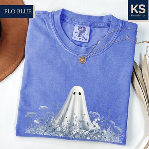 a blue t-shirt with a ghost design printed on it, along with a brown hat and some dried leaves.