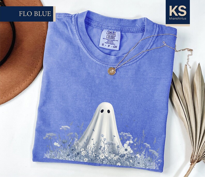 a blue t-shirt with a ghost design printed on it, along with a brown hat and some dried leaves.