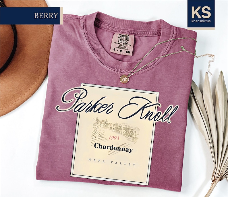 a pink t-shirt with a wine label design, a hat, and some dried leaves, all placed on a white background.