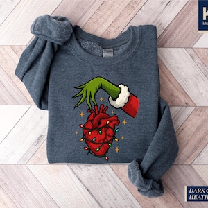 A gray sweatshirt with a graphic design depicting a hand holding a heart with Christmas lights around it.