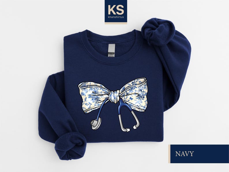 May include: Navy blue sweatshirt with a white and blue floral bow and a stethoscope design. The sweatshirt has a crew neck and long sleeves.