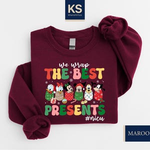 A burgundy-colored sweater with a Christmas-themed design featuring Disney characters and the text "we wrap the best presents #nuc".