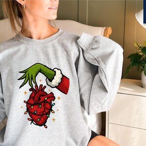 A woman wearing a grey sweatshirt with a graphic of a hand holding a heart with lights around it.
