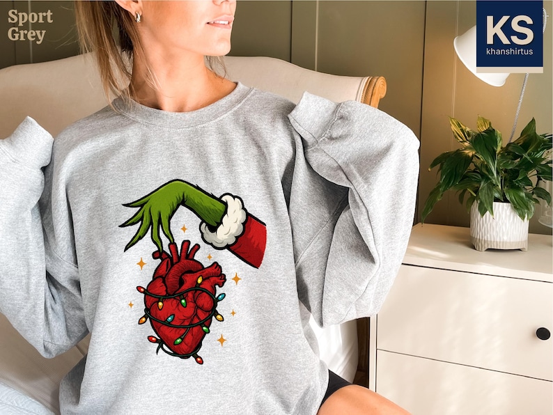 A woman wearing a grey sweatshirt with a graphic of a hand holding a heart with lights around it.