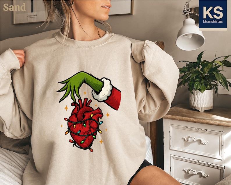 A woman wearing a beige sweater with a graphic of a hand holding a heart with lights around it.