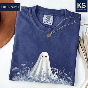 a blue t-shirt with a ghost design, a brown hat, and some dried leaves, all placed on a white surface.