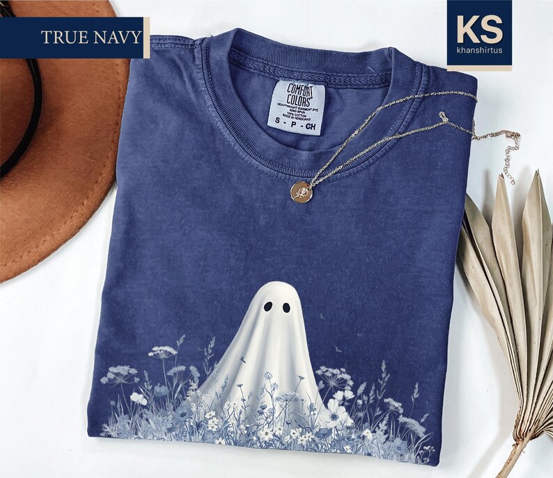 a blue t-shirt with a ghost design, a brown hat, and some dried leaves, all placed on a white surface.
