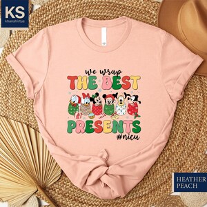 A pink t-shirt with a colorful graphic design featuring cartoon characters and text, placed on a woven mat.