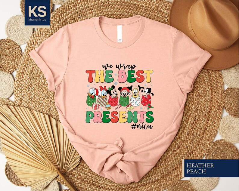 A pink t-shirt with a colorful graphic design featuring cartoon characters and text, placed on a woven mat.