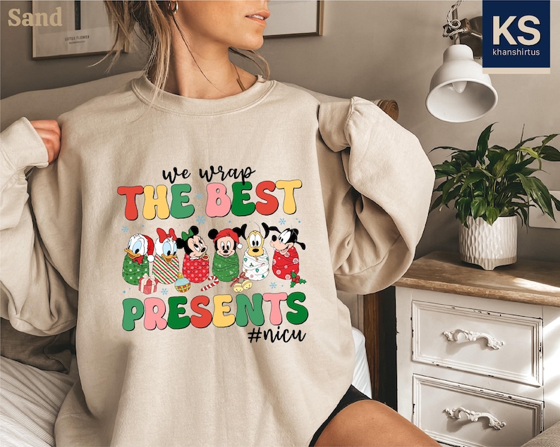 A woman wearing a beige sweater with a colorful graphic design featuring cartoon characters and text.