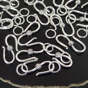 May include: A close-up of a group of silver-toned metal hooks with a small ball at the end of each hook. The hooks are scattered on a black surface.